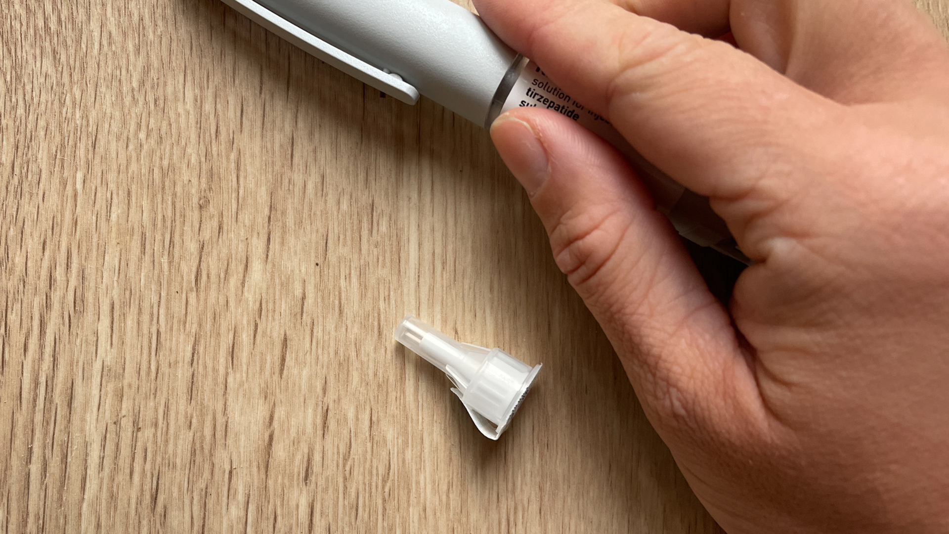 A person is holding a pen with a broken tip on a wooden table.