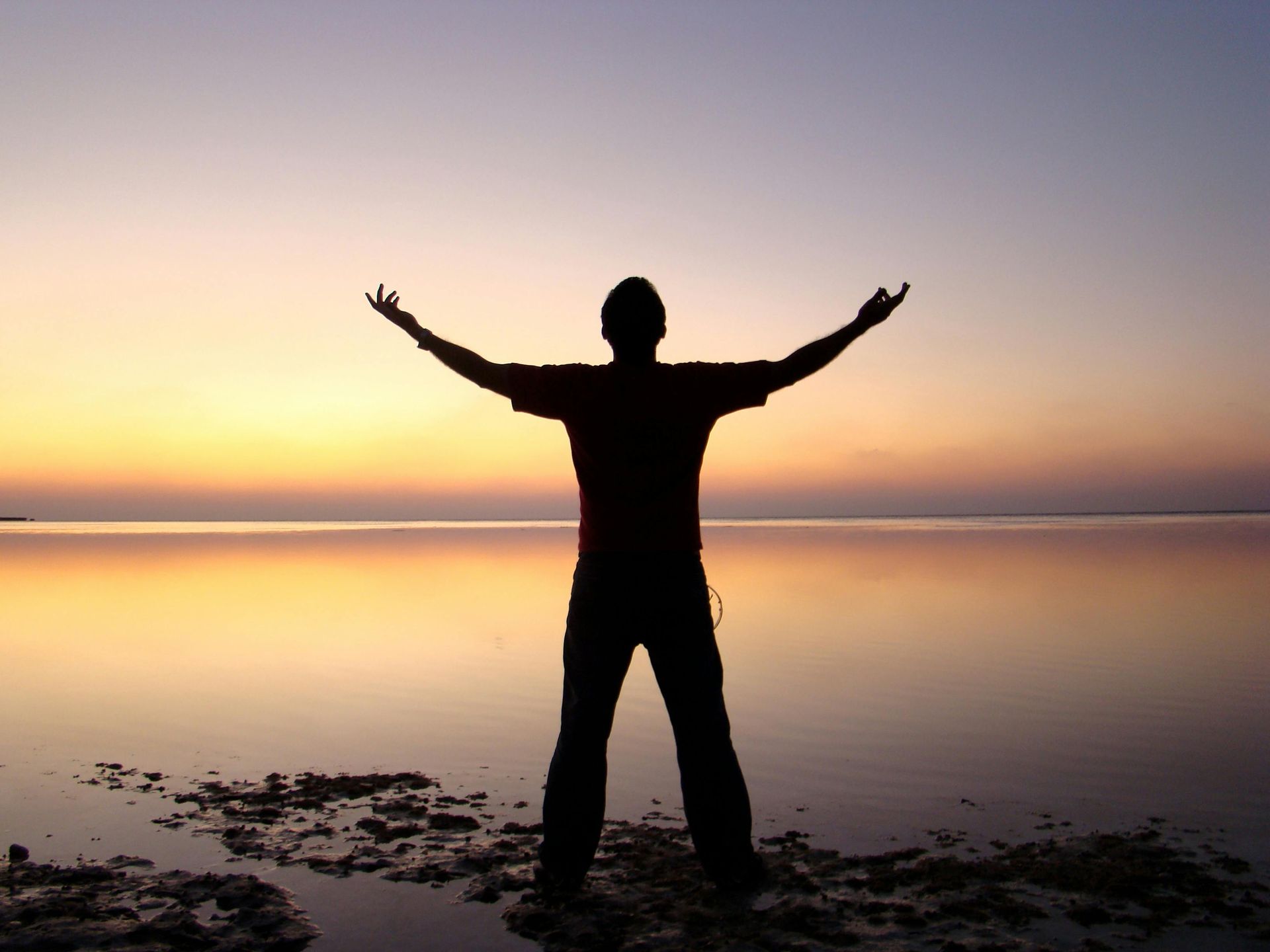 A silhouette of a man standing on a beach with his arms outstretched