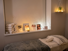 Cozy spa room with massage bed, rolled towels, candles, and warm wall lighting