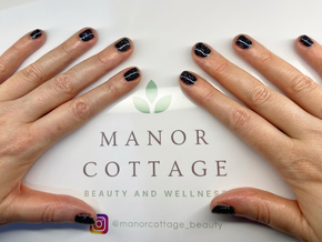 Hands with dark nail polish framing Manor Cottage Beauty and Wellness logo on a white background