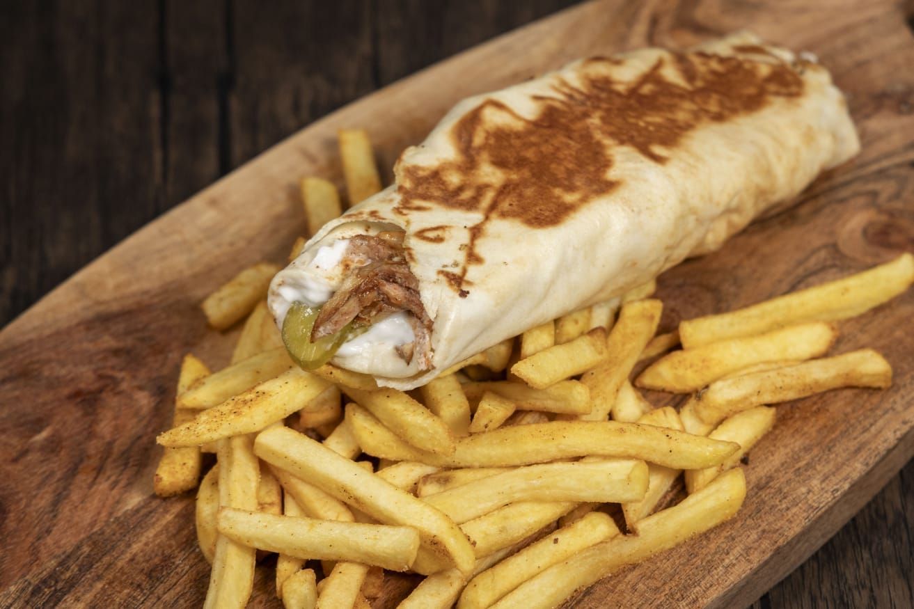 A burrito and french fries on a wooden cutting board.
