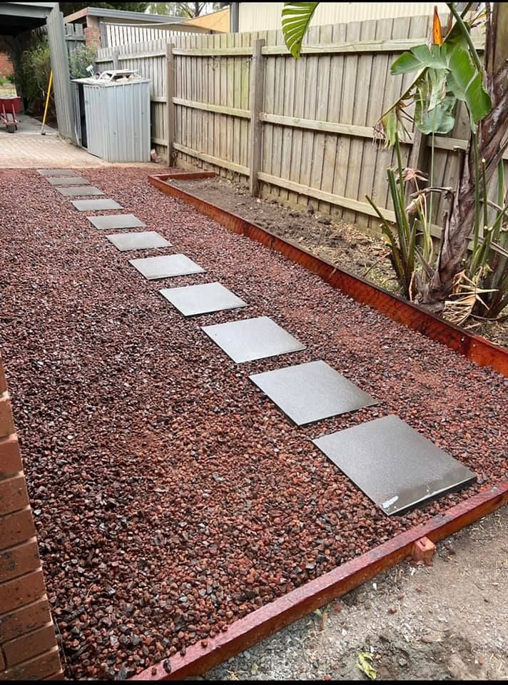 A row of stepping stones leading to a wooden fence in a backyard.
