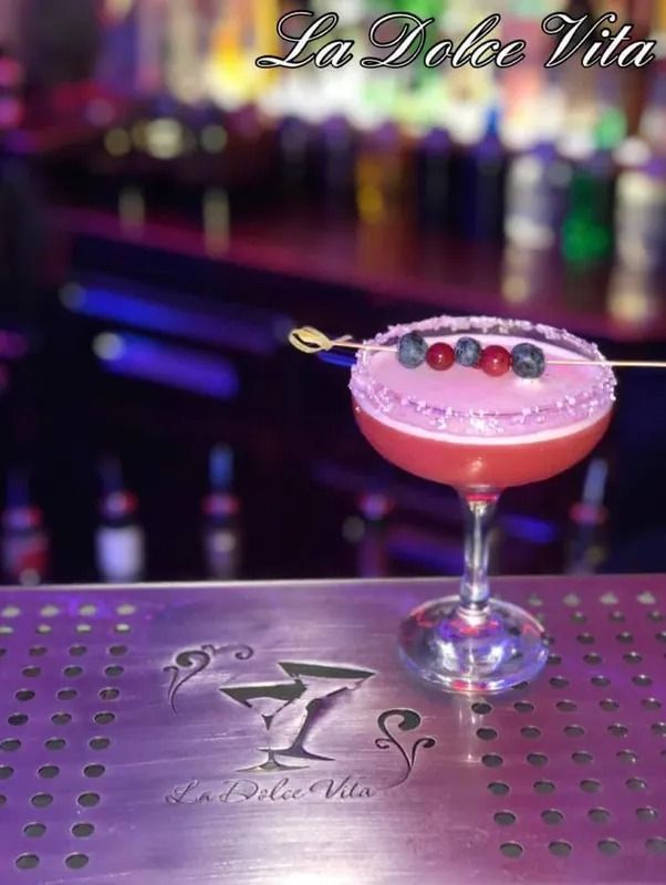 Cocktail con schiuma rosa in un bicchiere da cocktail, guarnito con frutti di bosco, su un bancone con il logo 