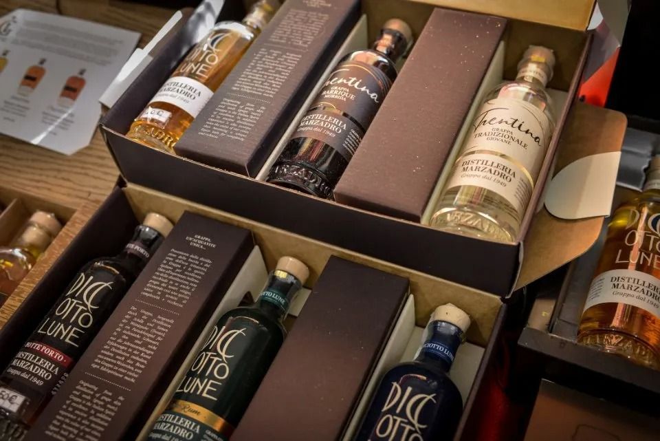 Bottiglie di liquore in scatole regalo, di vari colori, esposte su un bancone, presumibilmente in vendita.