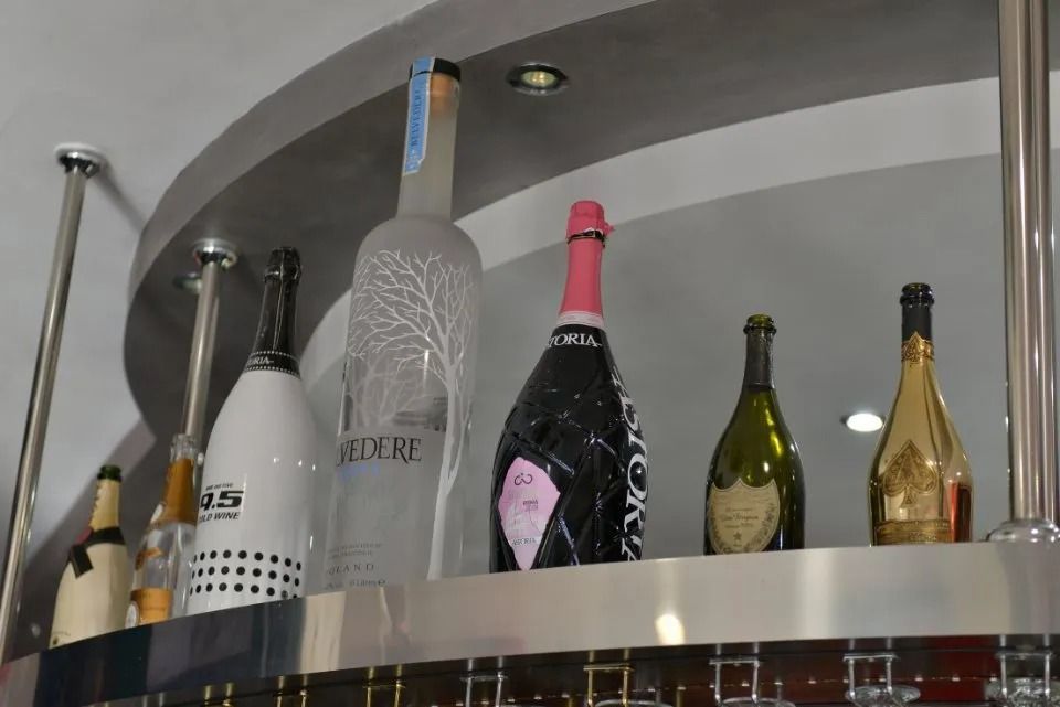Bottiglie di alcolici esposte sullo scaffale di un bar; tra cui vodka, champagne e vino.