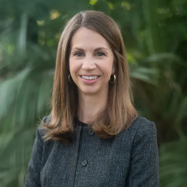 A woman in a gray jacket and earrings is smiling for the camera.