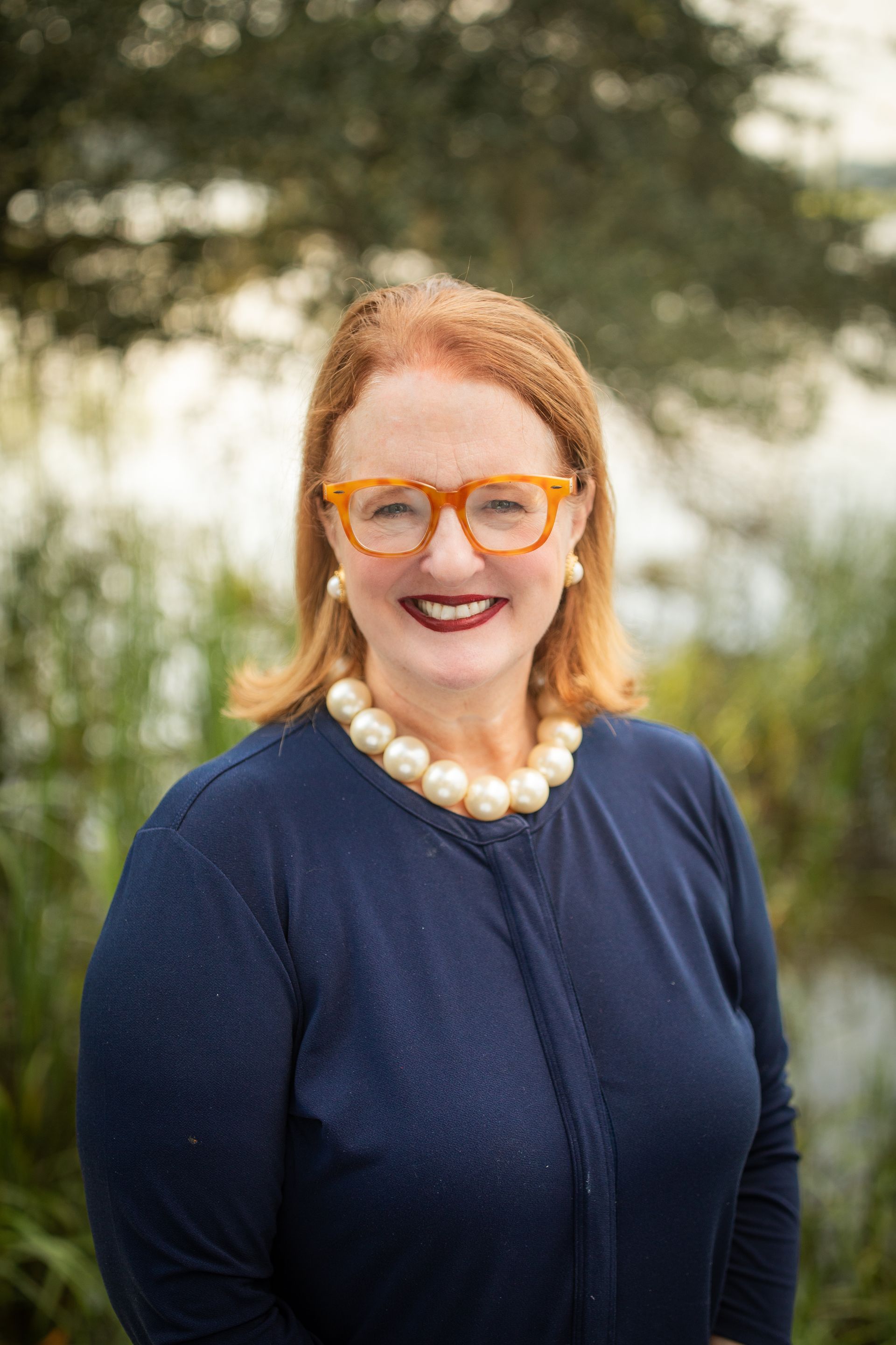 A woman wearing glasses and a black jacket is standing in the woods.