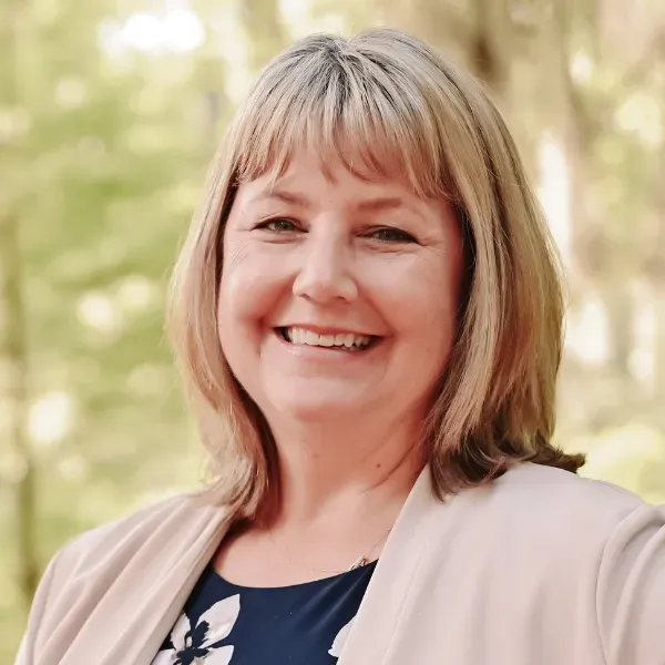 A woman is smiling for the camera while wearing a jacket and a blue dress.