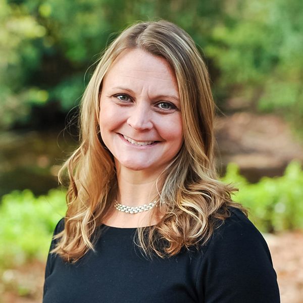 A woman wearing a black shirt and a necklace is smiling for the camera.