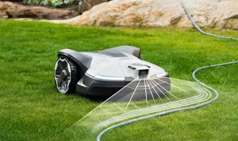 Ein Mähroboter auf einem grünen Rasen erkennt einen Gartenschlauch mithilfe eines digitalen Sensorgitters.