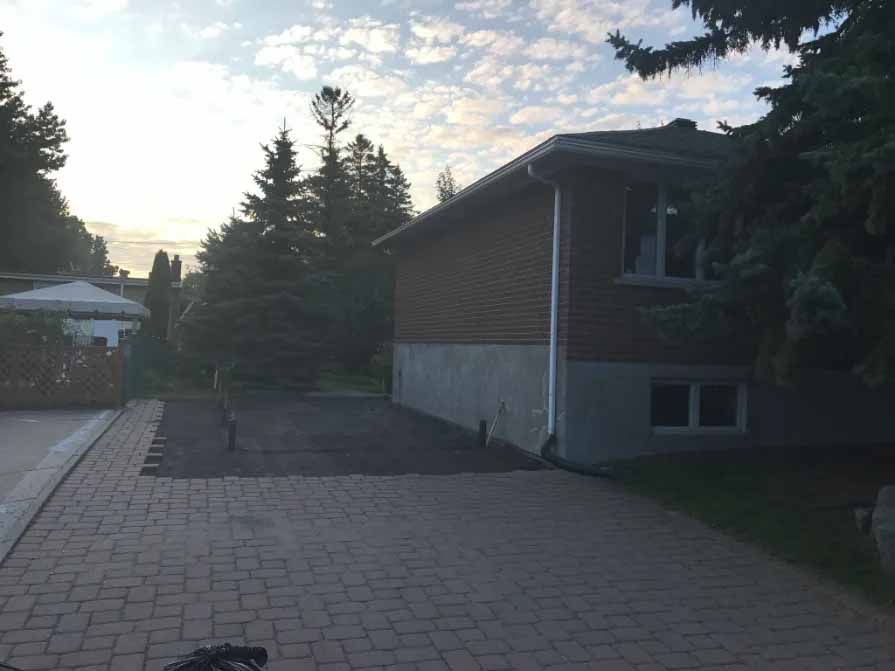 Maison en briques avec allée et arbres sous un ciel nuageux.