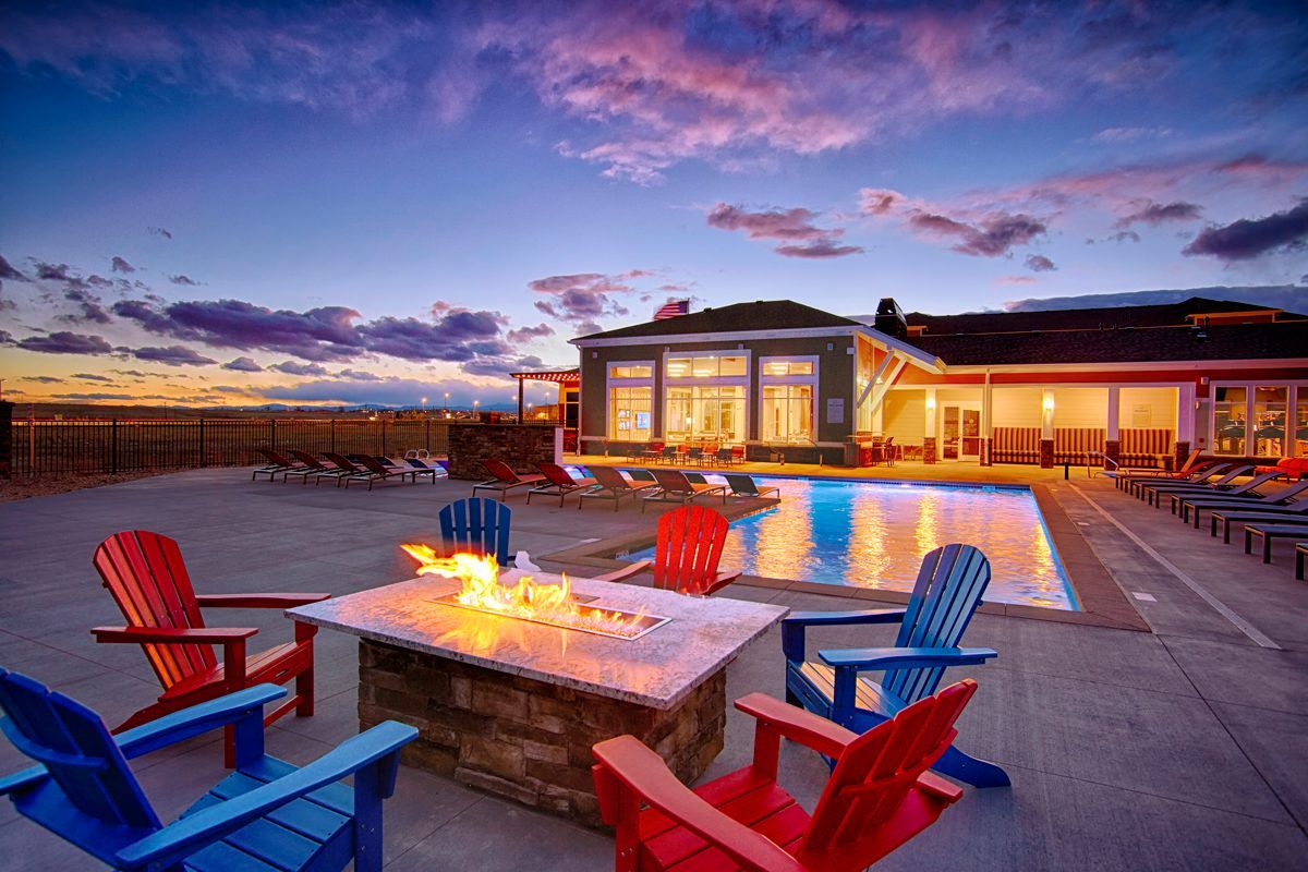 Poolside fire pit with colorful chairs, pool, and building at dusk.