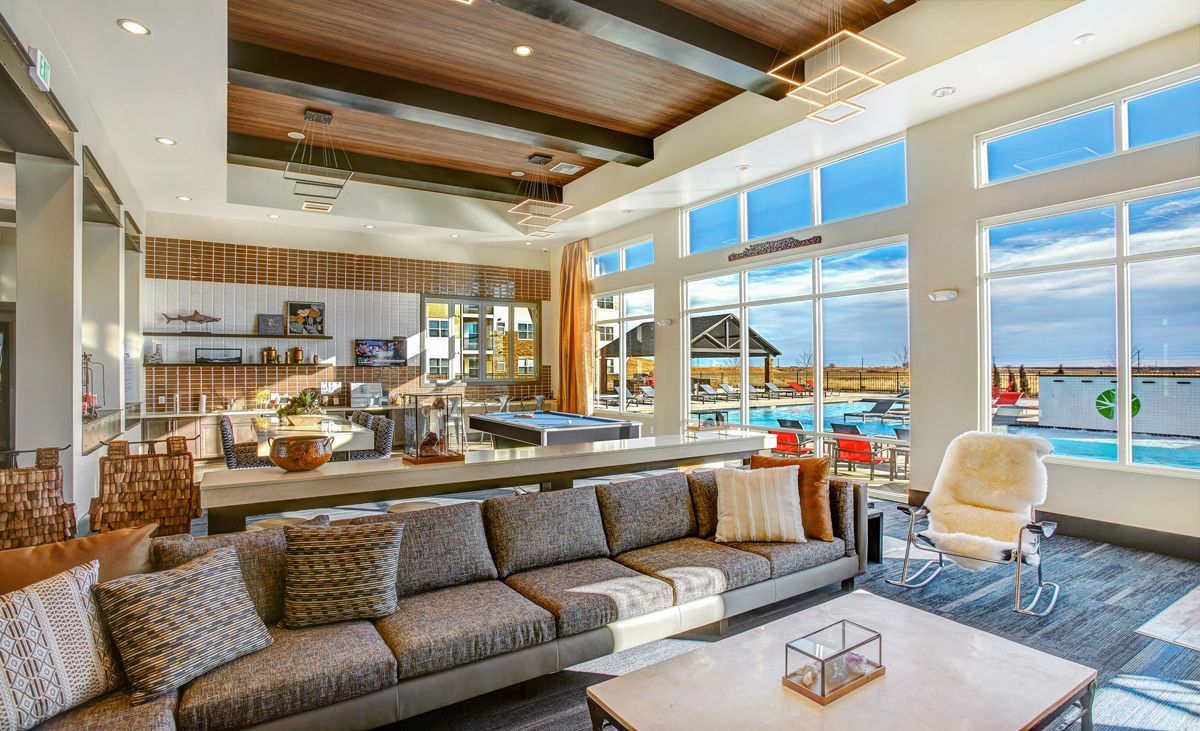 Lounge area with a large sofa, windows overlooking a pool, wood ceiling, and modern decor.