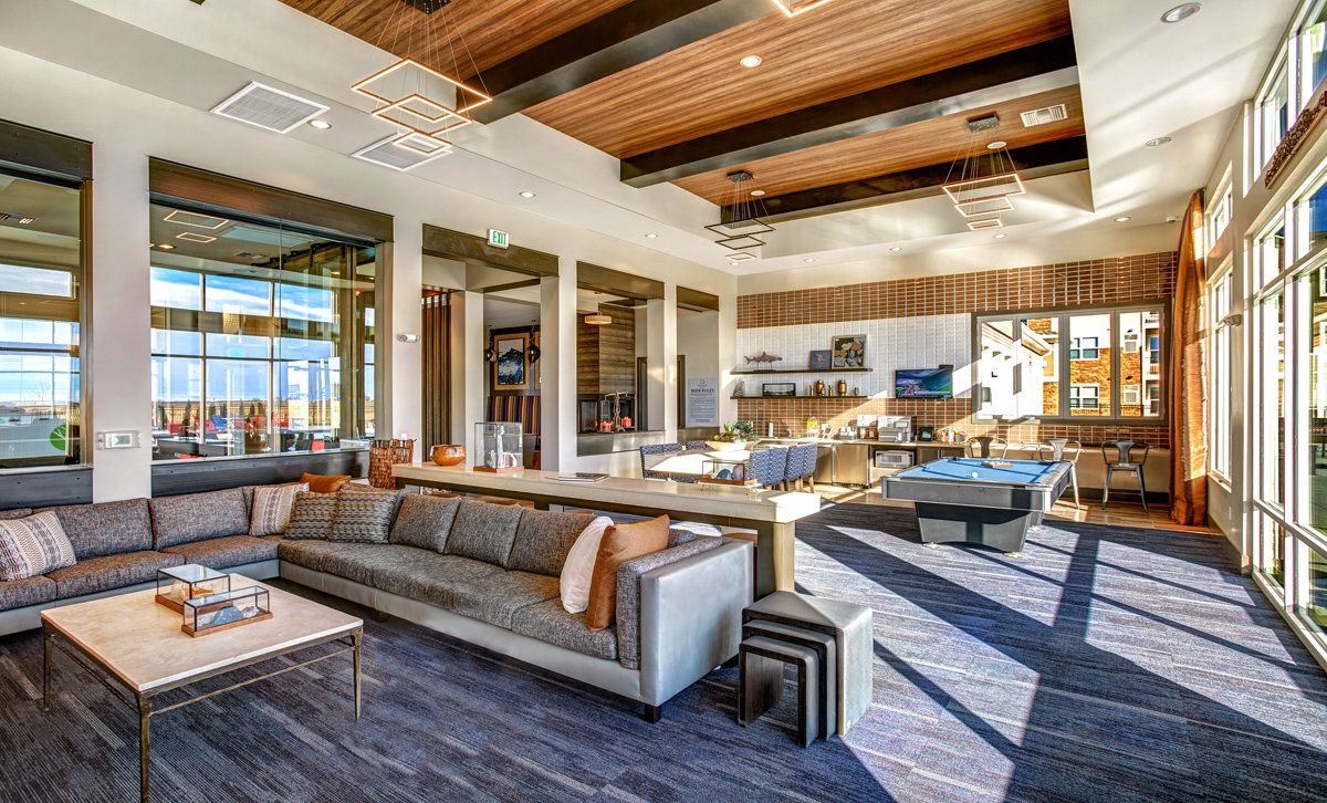 Modern lounge with large windows, sofas, pool table, wood ceiling and accent wall; sunlit.