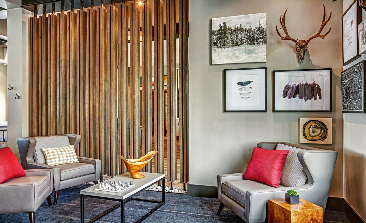 Lounge area with gray sofas, red pillows, art, wooden slat wall, and antlers mounted on a gray wall.