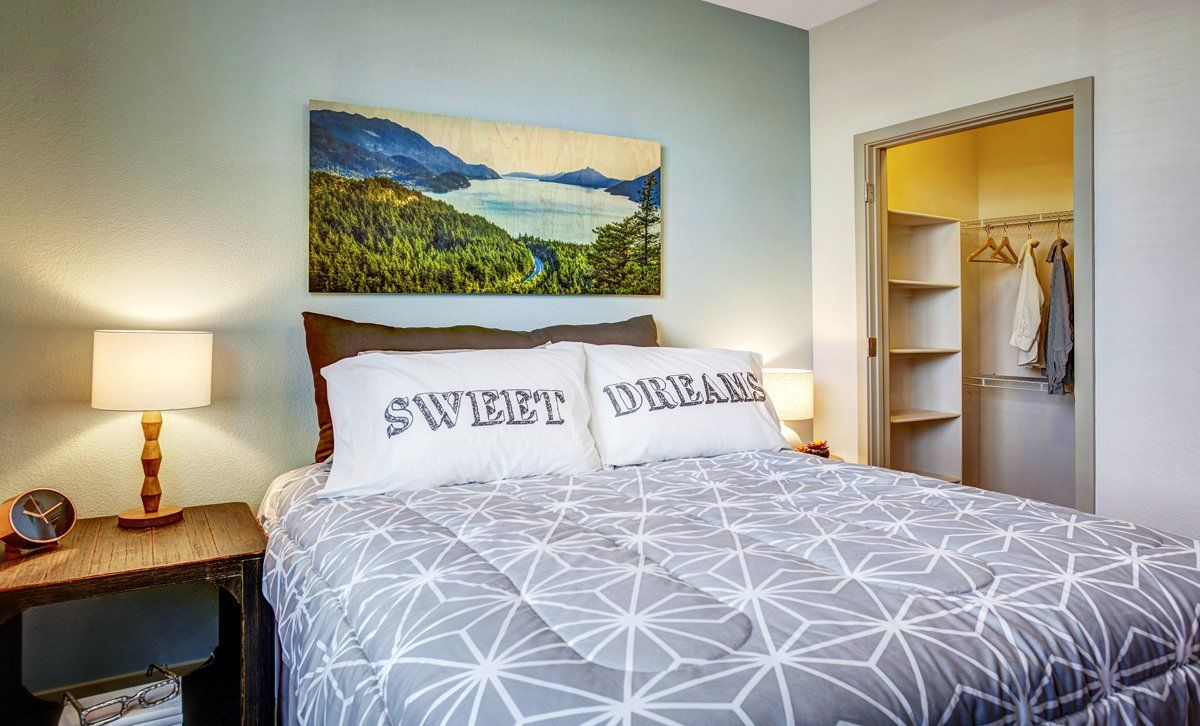 Bedroom with bed, nightstands, closet, and landscape art on the wall. Light blue wall color.