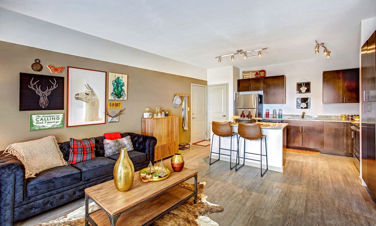 Living room with a kitchen in the background. Features a dark sofa, art on the wall, and a wood coffee table.