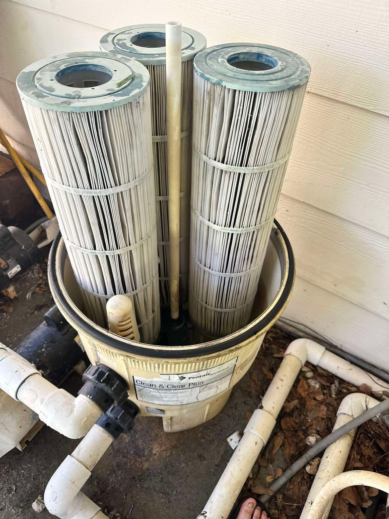 Pool filter with three cartridge filters inside a beige housing, with pipes attached.