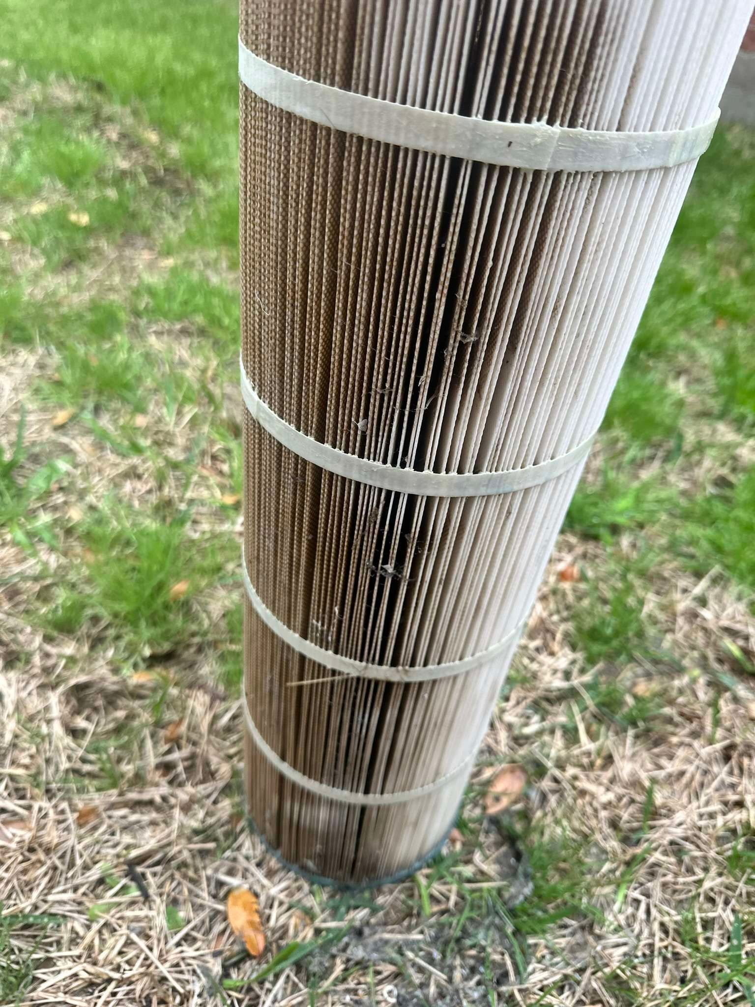Dirty cylindrical pool filter on grass. White pleated filter with dark grime.