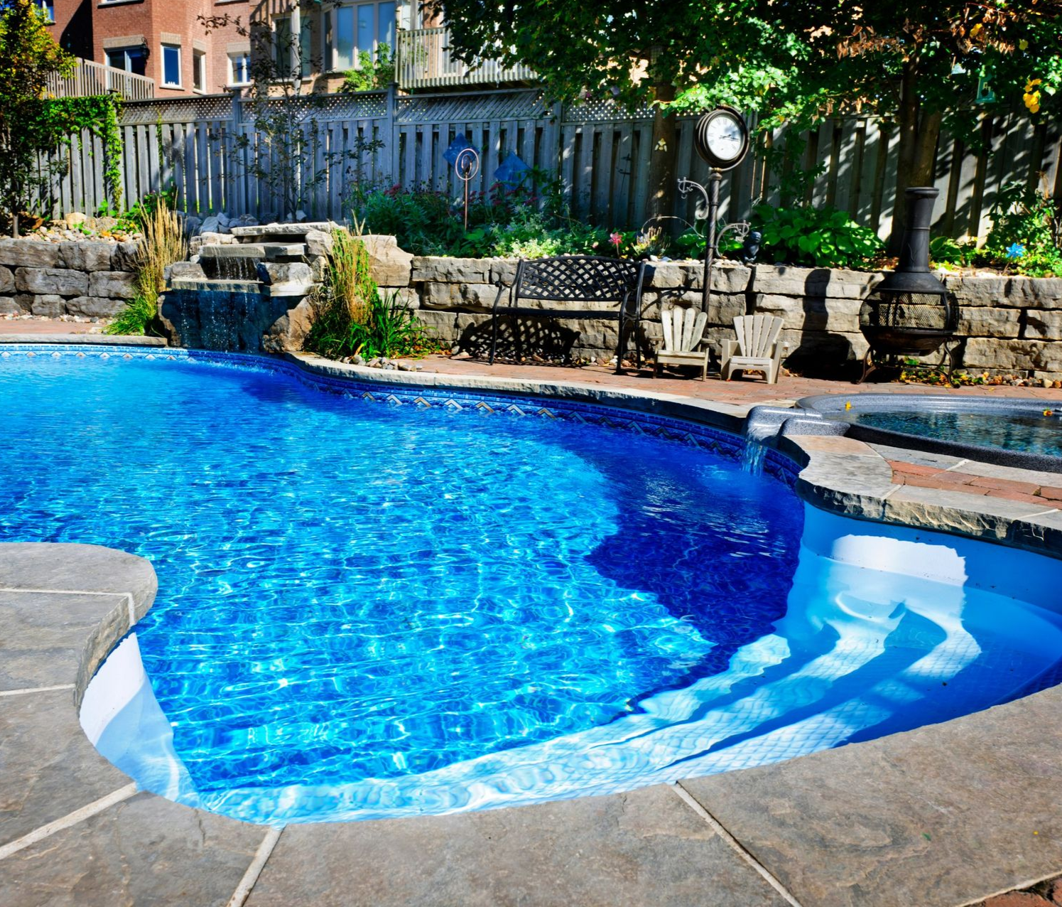 Backyard pool with a waterfall feature, hot tub, and brick patio.