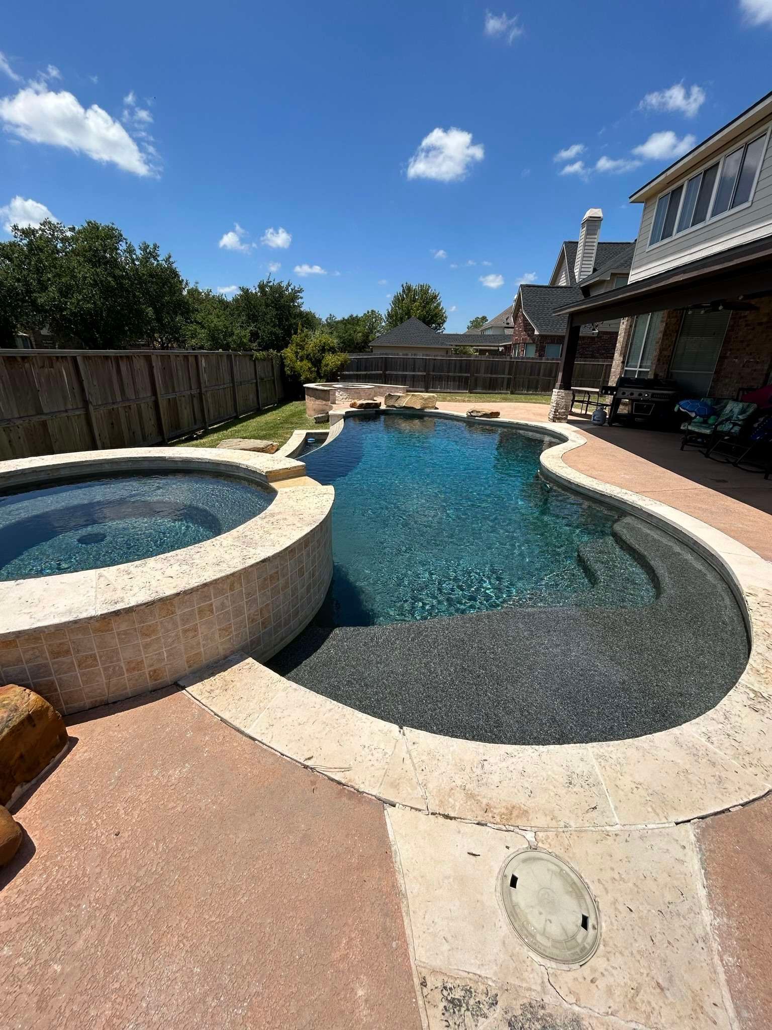 A backyard swimming pool and hot tub on a sunny day.