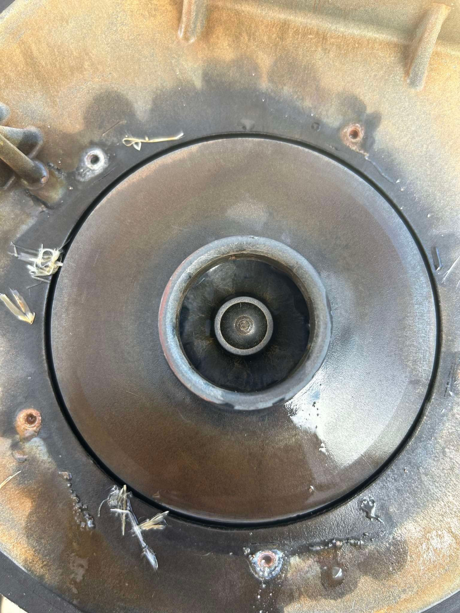 Close-up of a circular, dark, metallic impeller with a central shaft and surrounding debris.