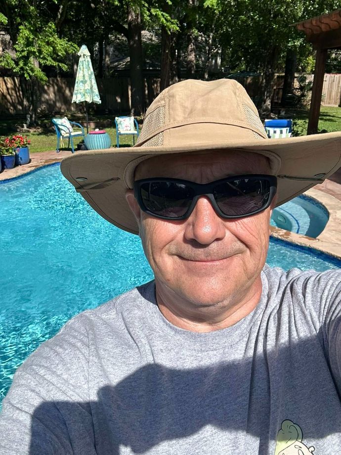Man in sunglasses and hat by a pool on a sunny day.