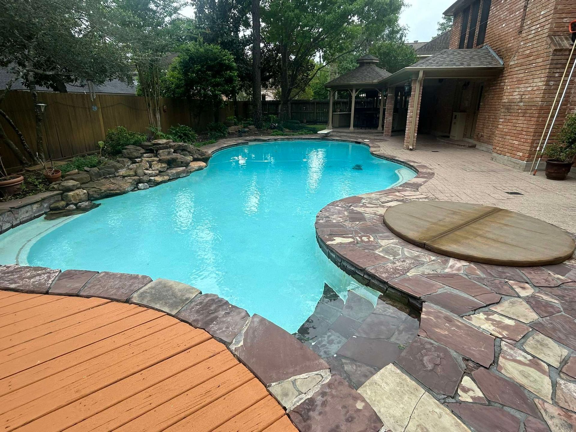 A blue-tiled swimming pool and spa surrounded by stone and a wooden deck in a backyard setting.