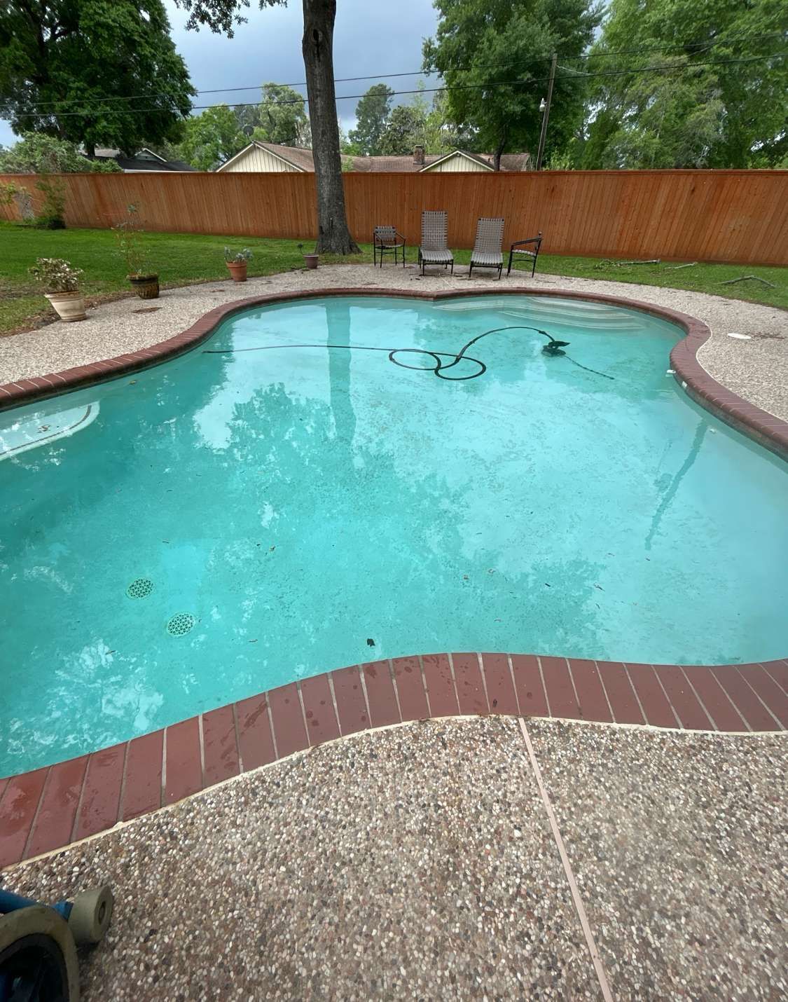 Swimming pool with turquoise water, surrounded by brick and textured concrete. Wooden fence in background.