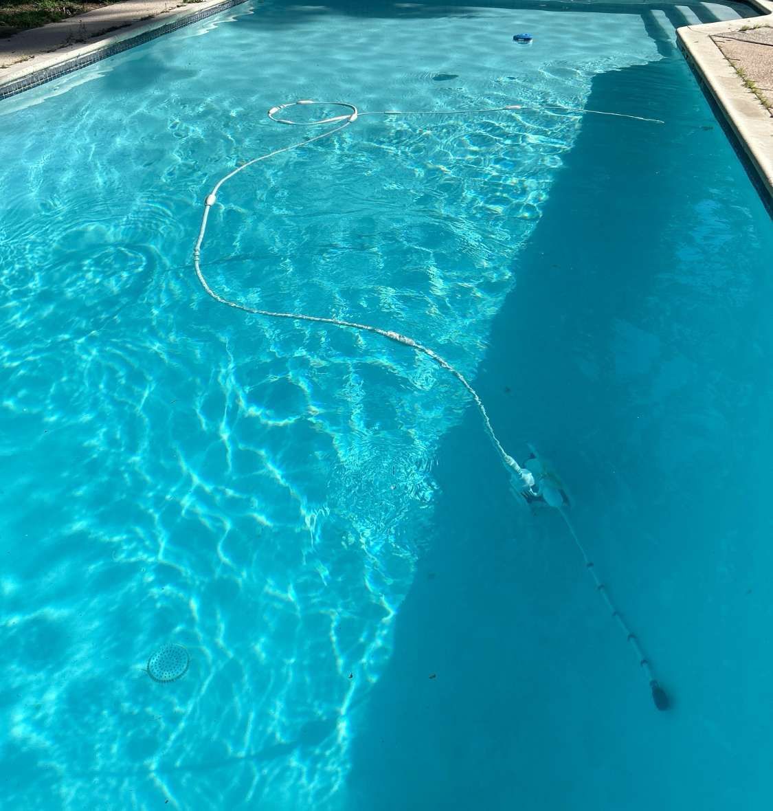 Pool filled with bright blue water, with a robotic cleaner hose and bubbles.