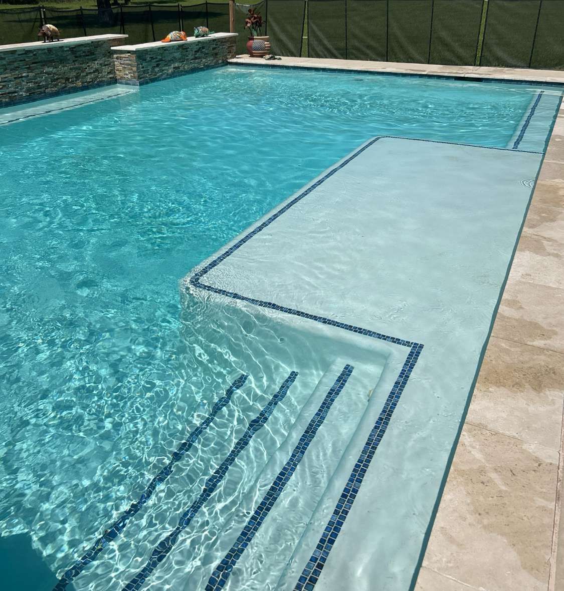 Swimming pool with steps, blue water, and stone deck, edged with dark blue tile.