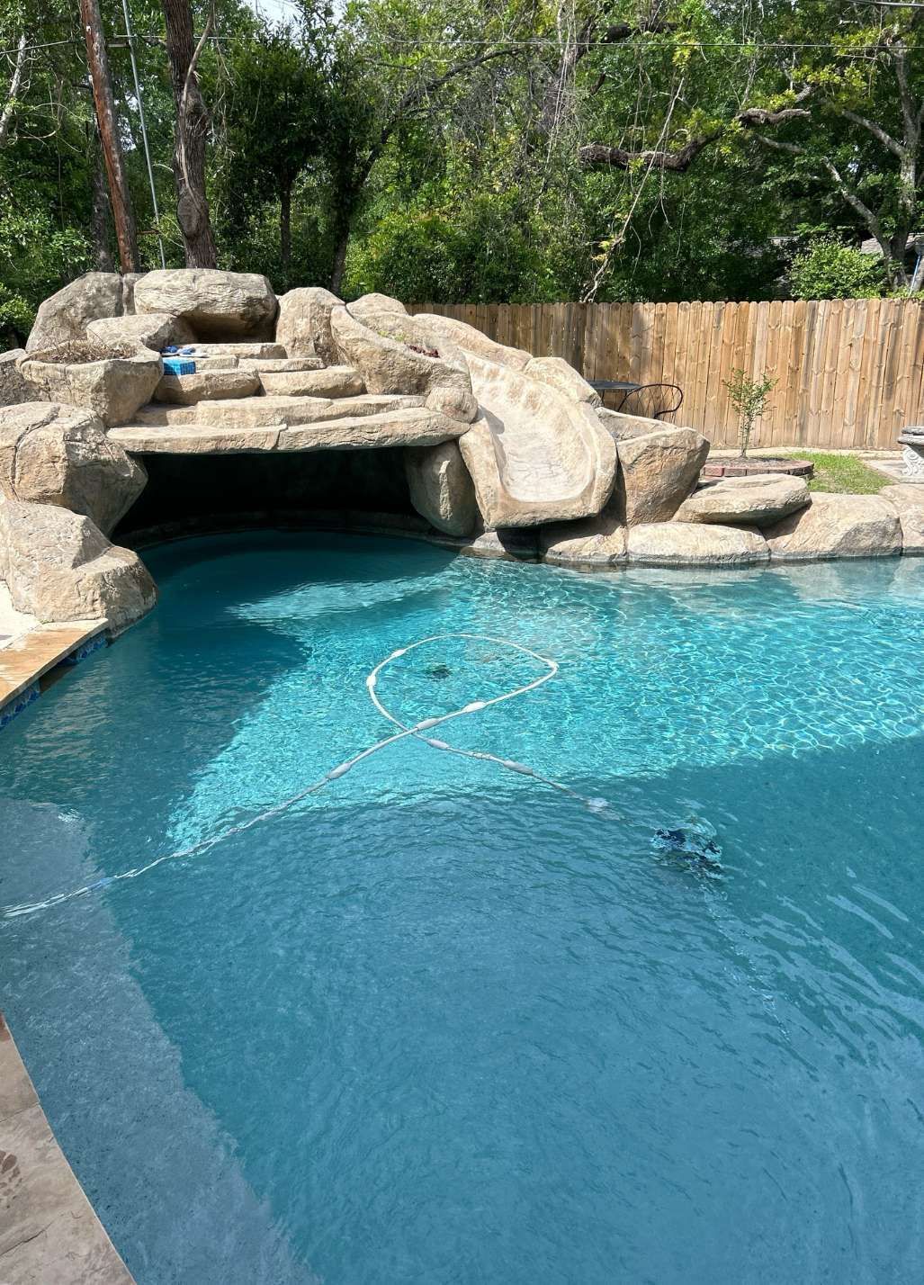 Swimming pool with a rocky waterfall feature, blue water, and a bamboo fence.