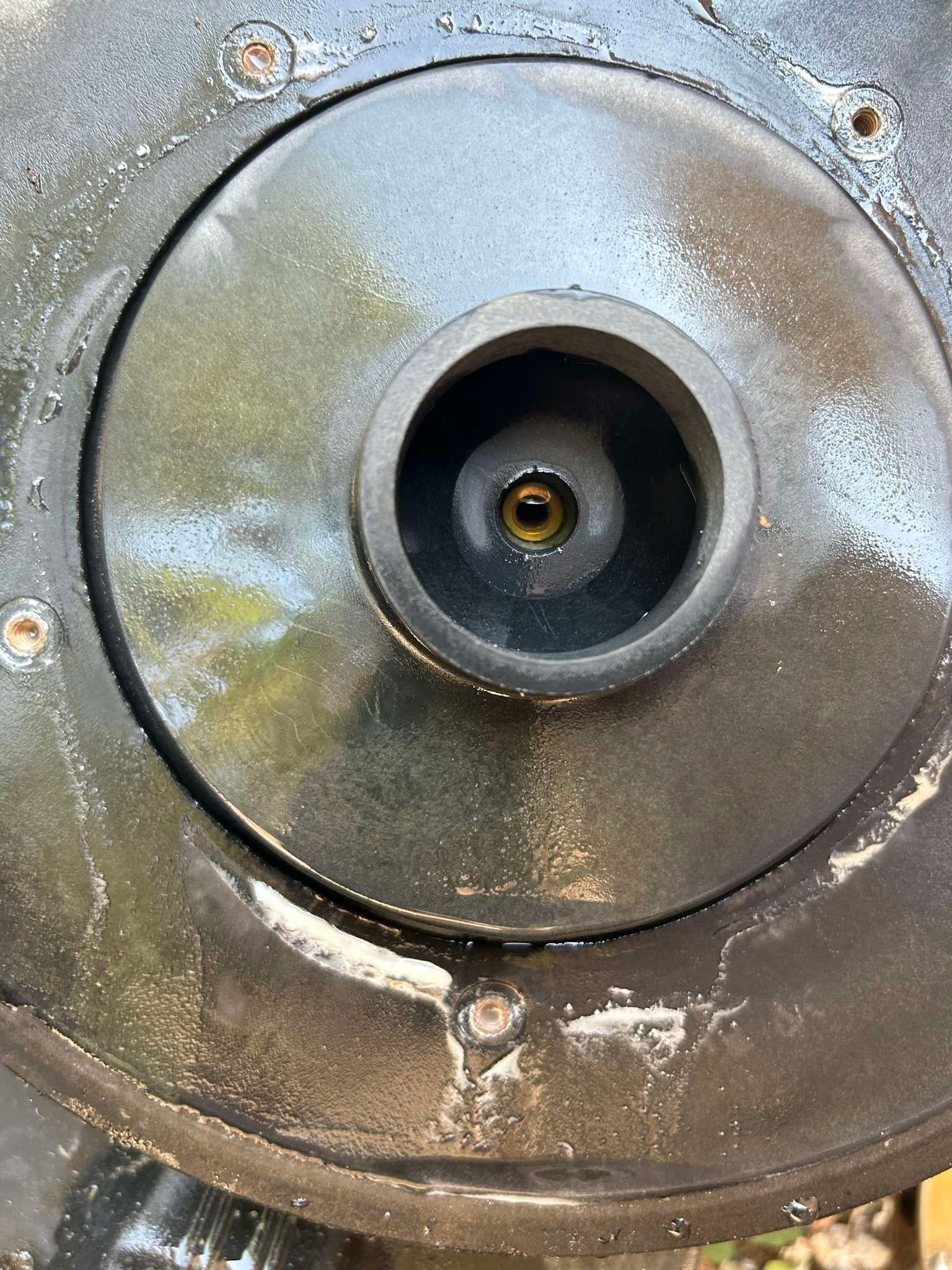 Black, circular object with a central, recessed opening containing a small, golden-brown liquid.