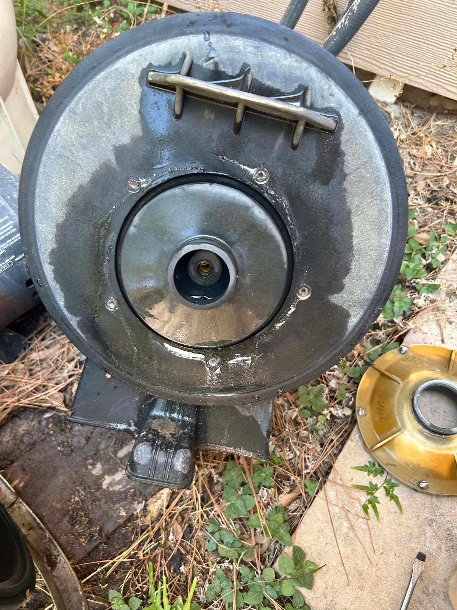 Black, circular pool pump component with central fitting, metal bar, and visible water residue.