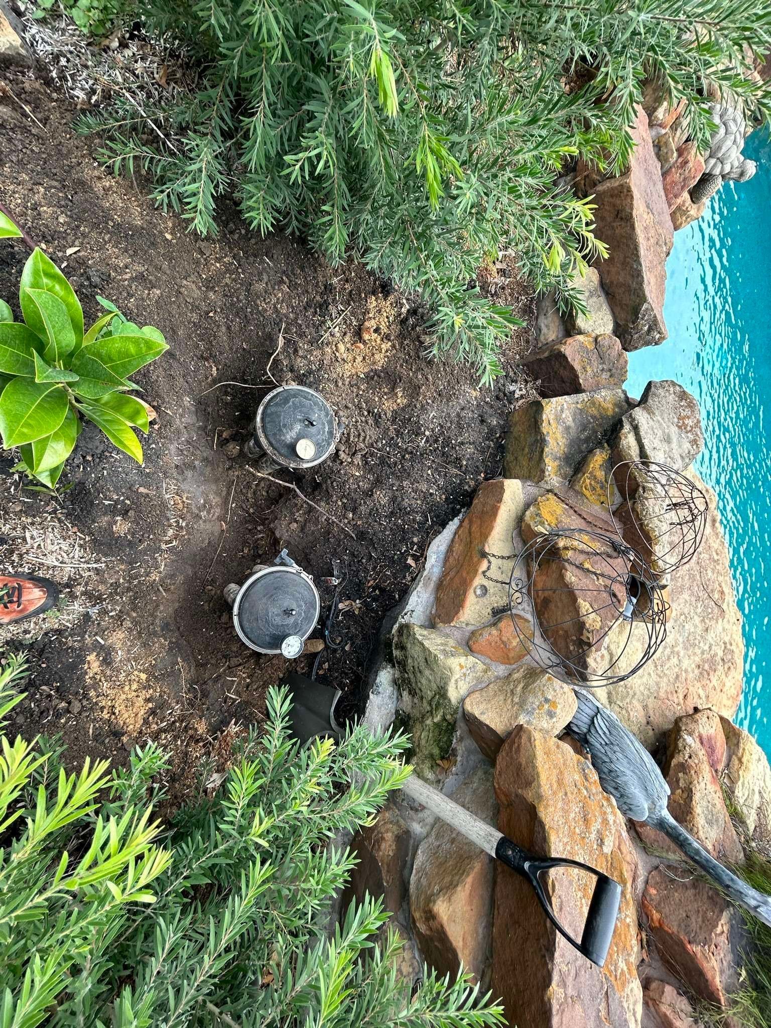 Garden bed with three irrigation heads near a stone retaining wall and pool.