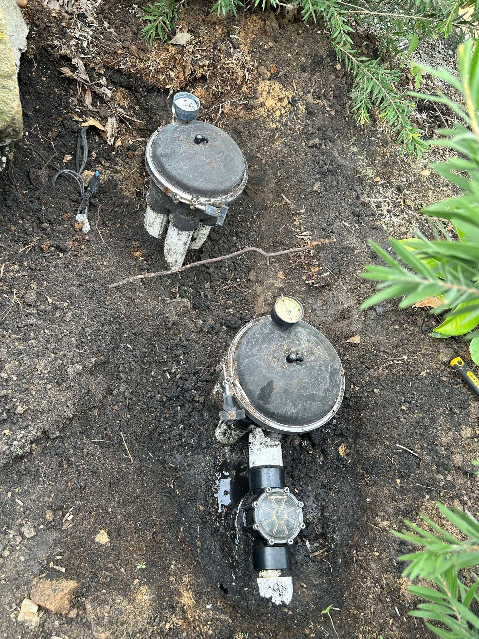 Two black irrigation control valves in soil.