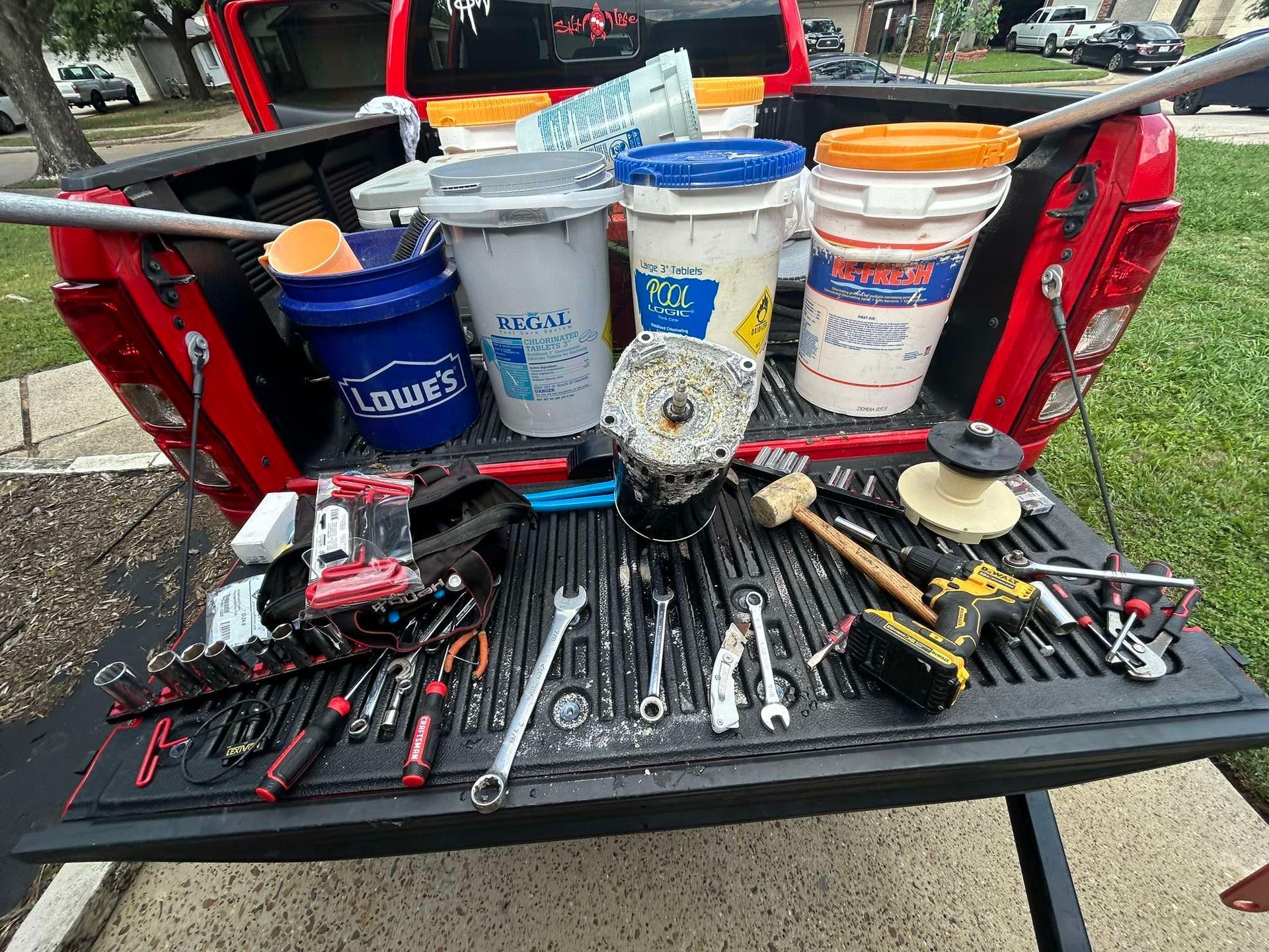 Red truck bed filled with buckets, tools, and a motor.