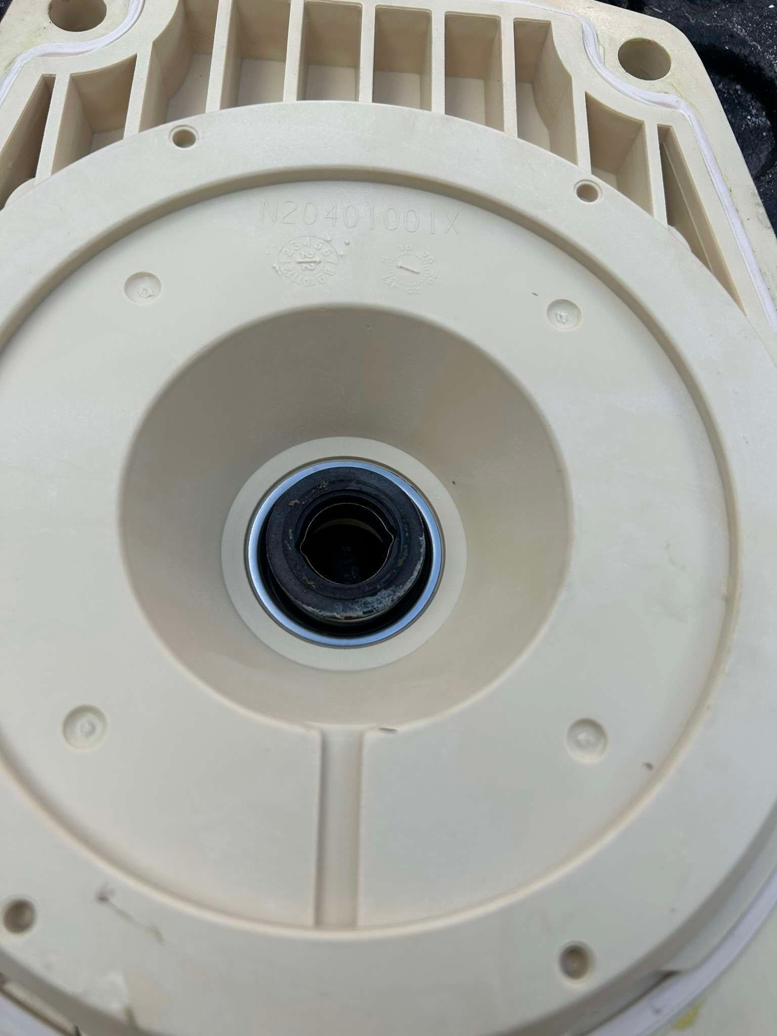 Off-white pump housing interior with a black shaft opening, surrounded by several screw holes.