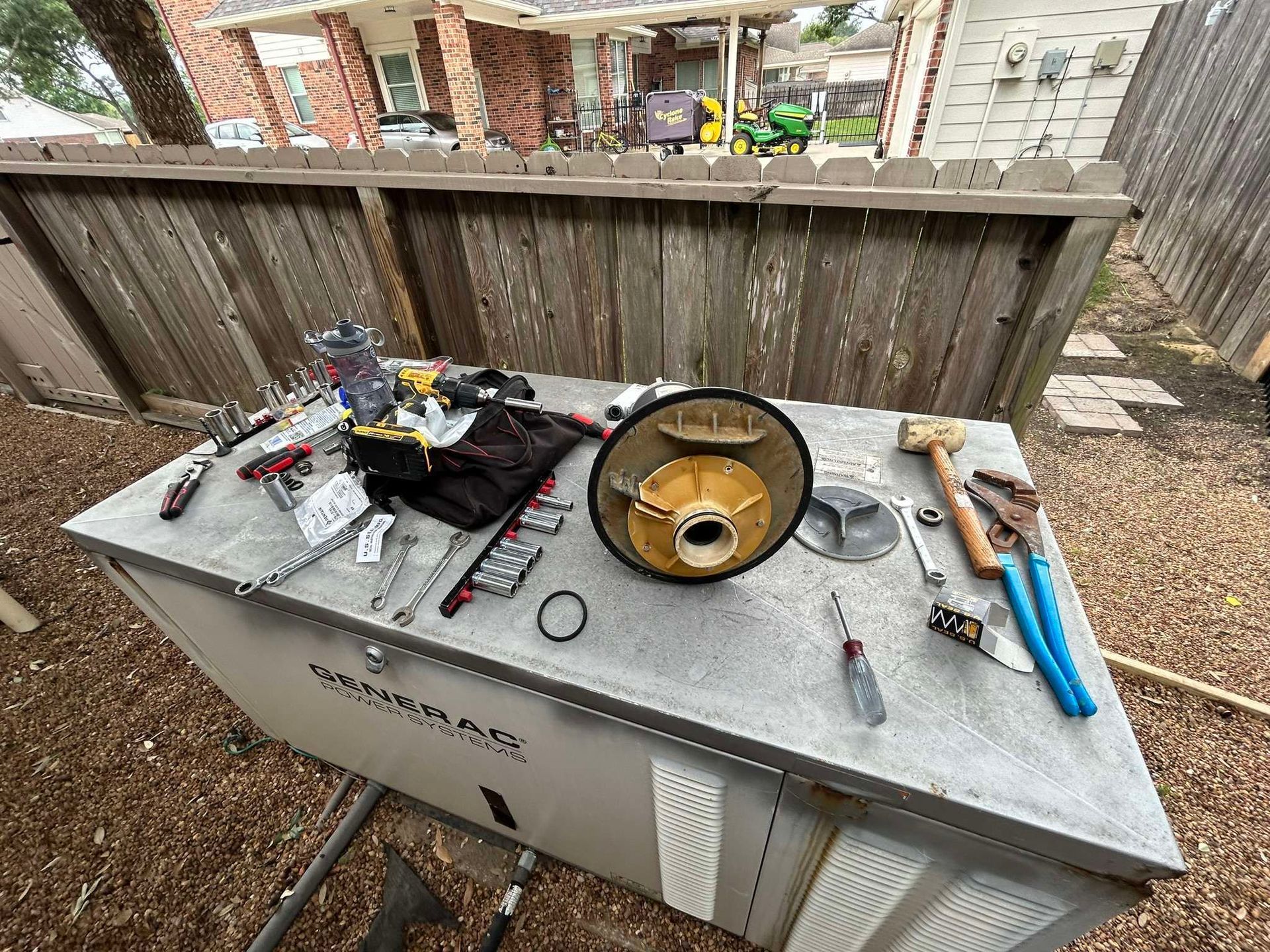 Tools and generator parts on a metal surface outside near a wooden fence.
