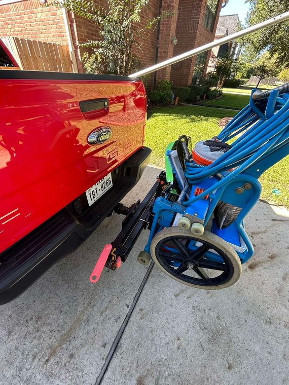 Red truck's bumper next to blue power washer on a concrete driveway.