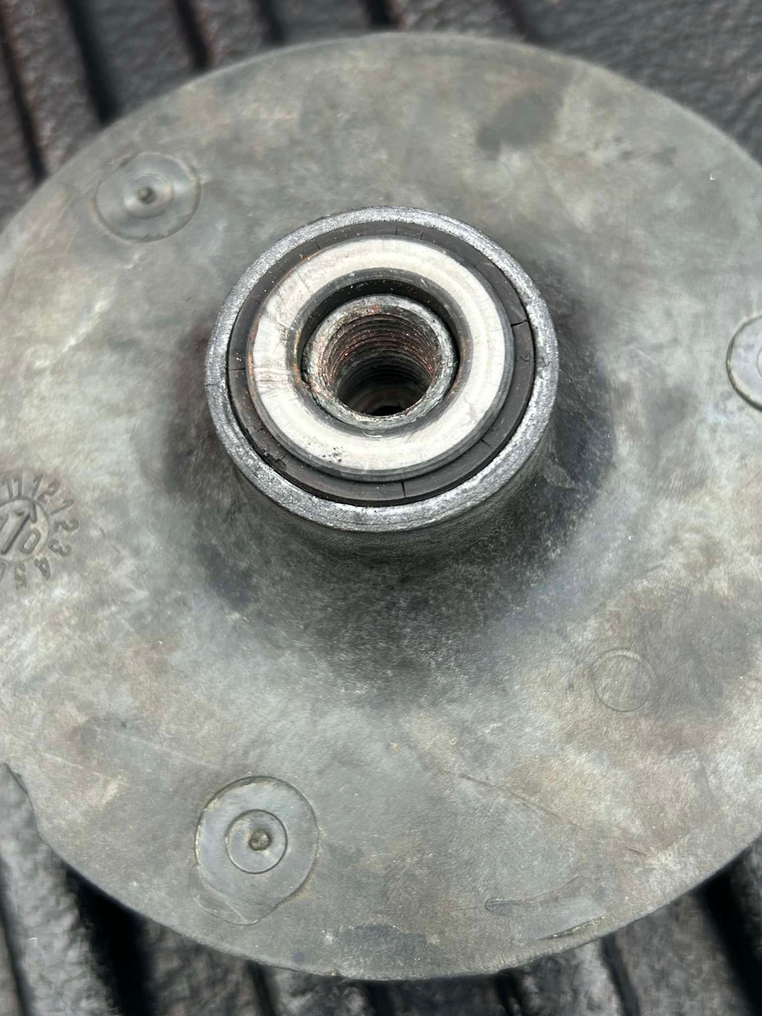 Circular, gray metal part with a central hub containing a bearing. Surface has three small circular indentations.