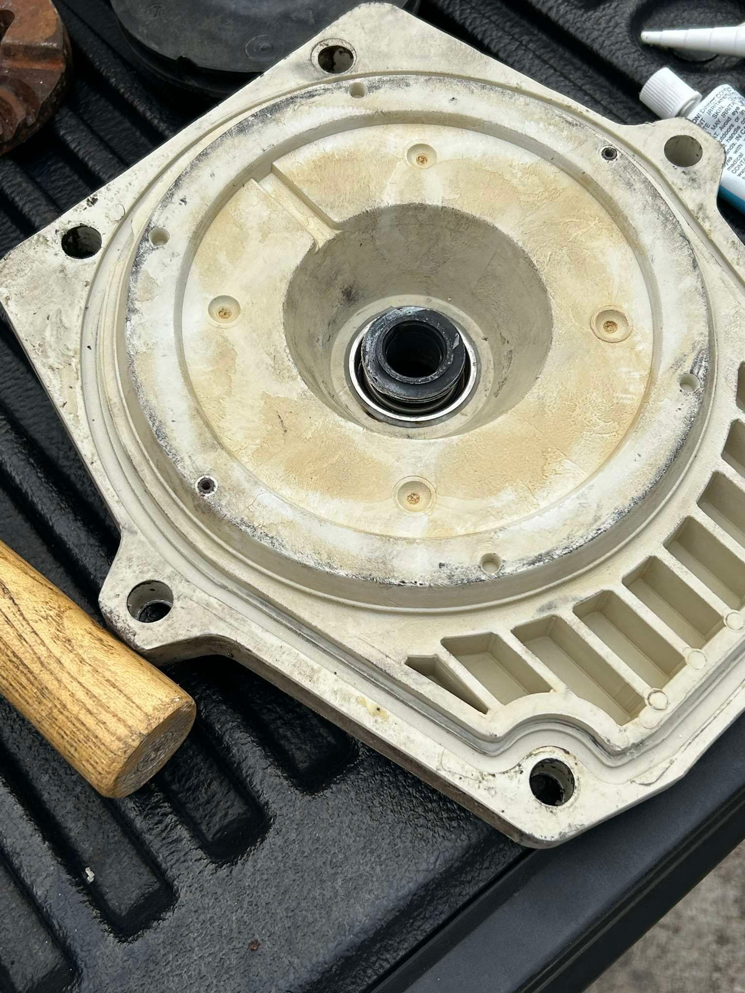 White pump part with central black bearing and surrounding residue; a hammer rests nearby.