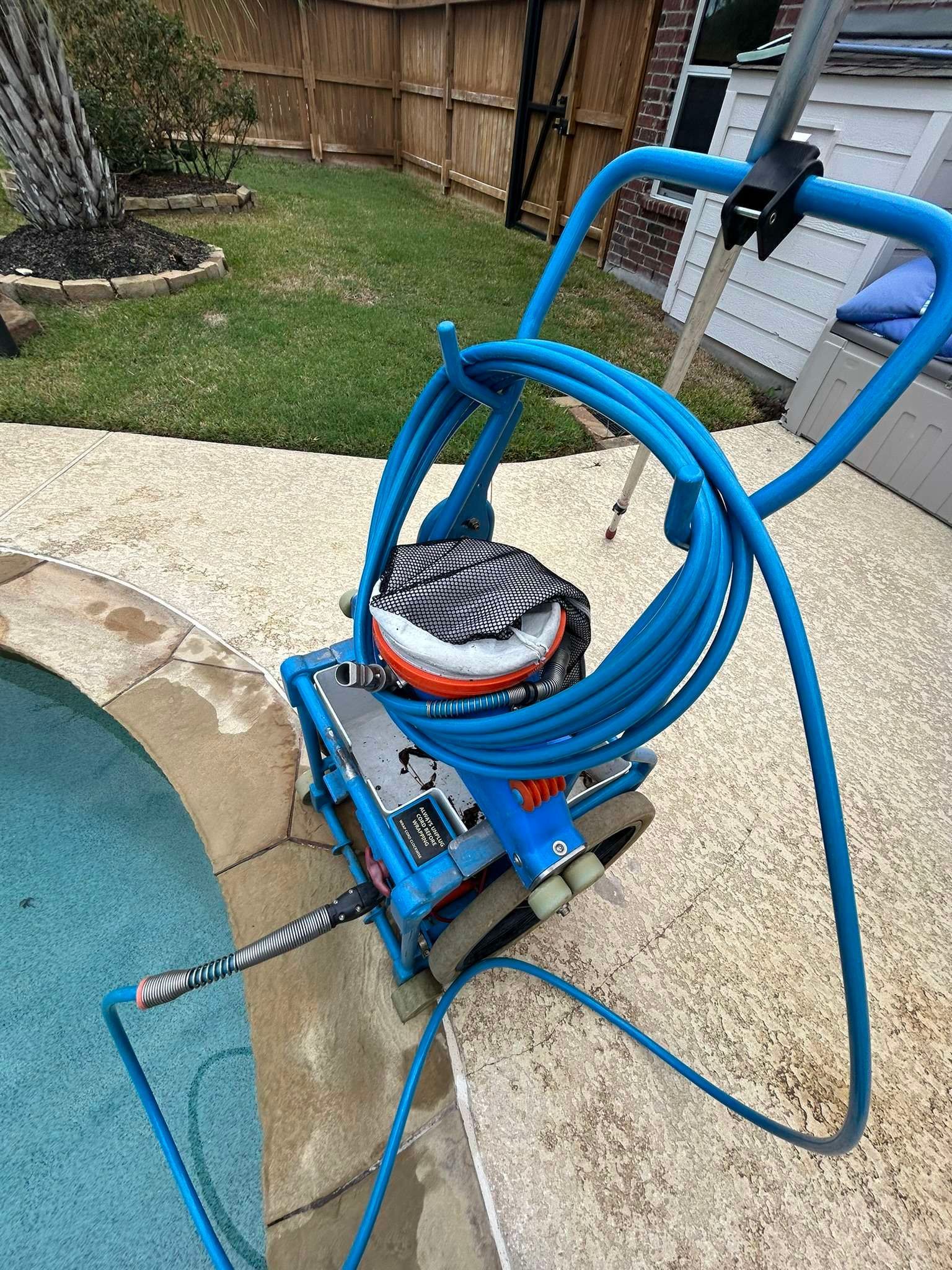 Blue robotic pool cleaner on pool deck next to a pool.