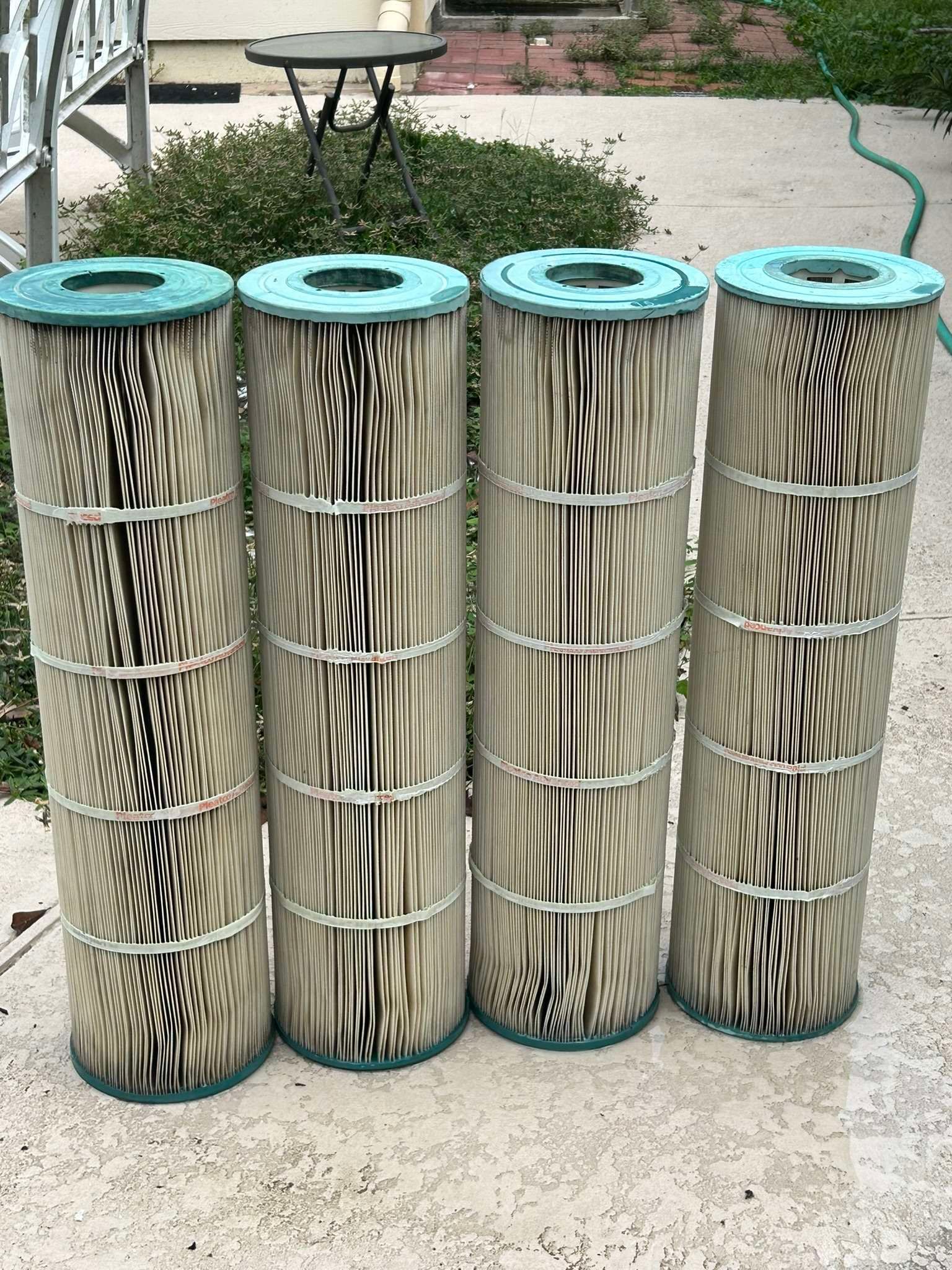 Four cylindrical pool filters, beige and vertically ribbed with green tops, stand outdoors.