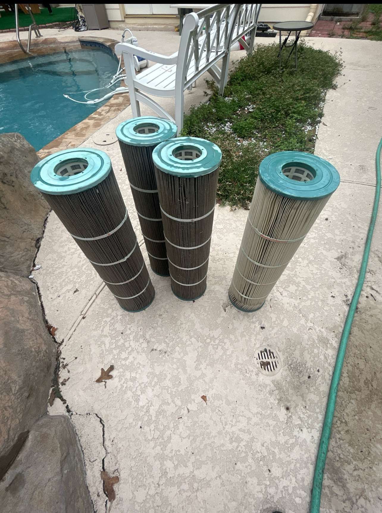 Four dirty pool filter cartridges on concrete by a pool.