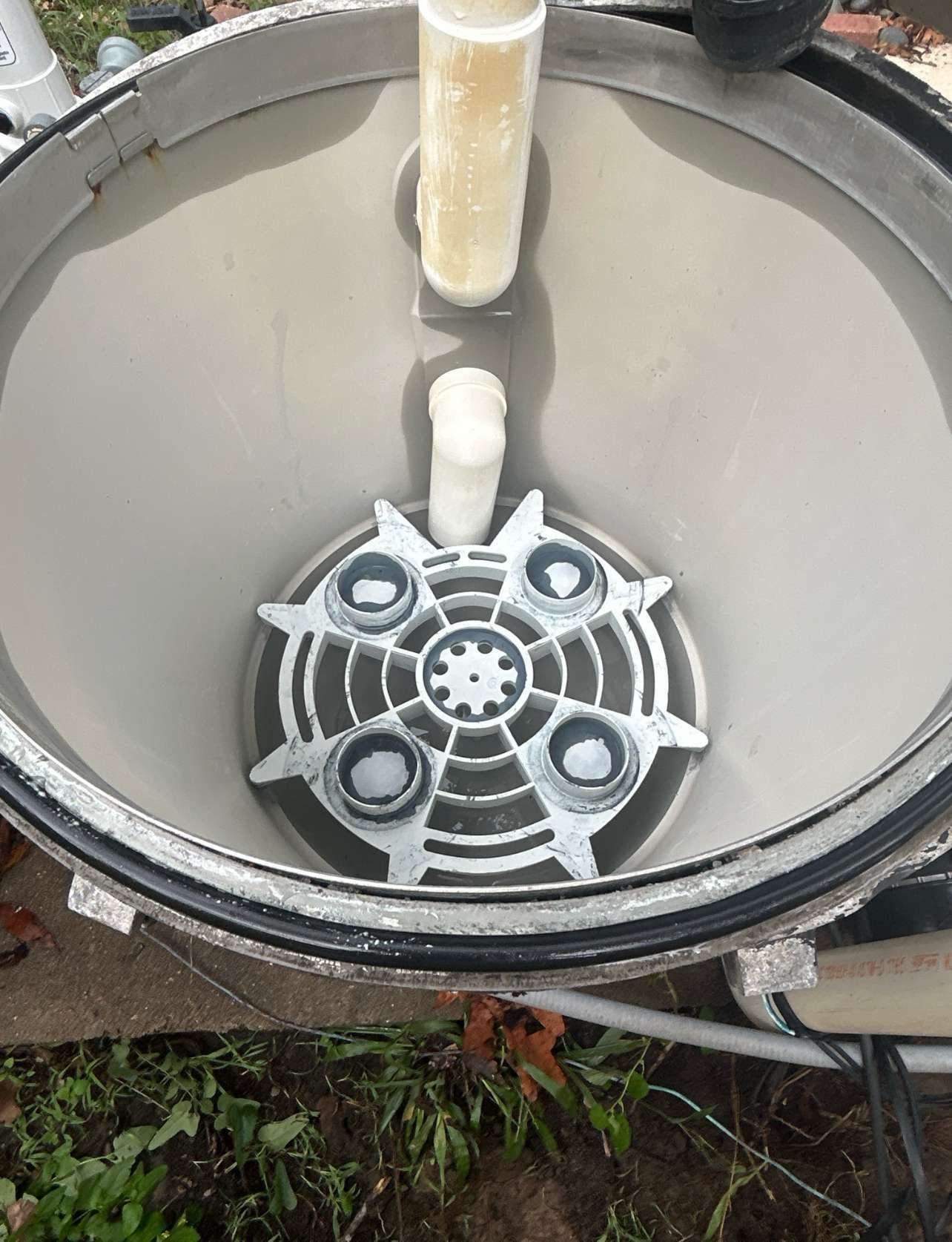 Inside view of a pool filter with a circular grate and connected pipes. Gray, beige, and white colors are present.