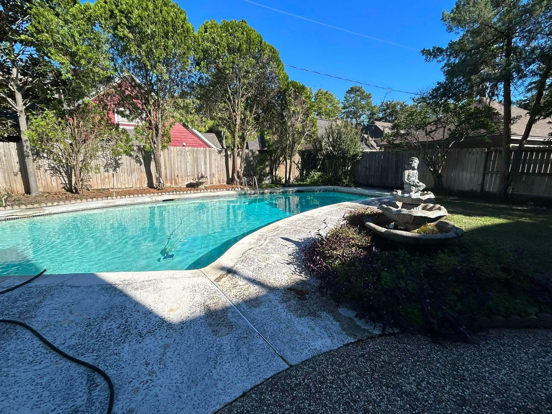Backyard pool with stone deck and landscaping. A fountain is to the right with a wooden fence in the background.