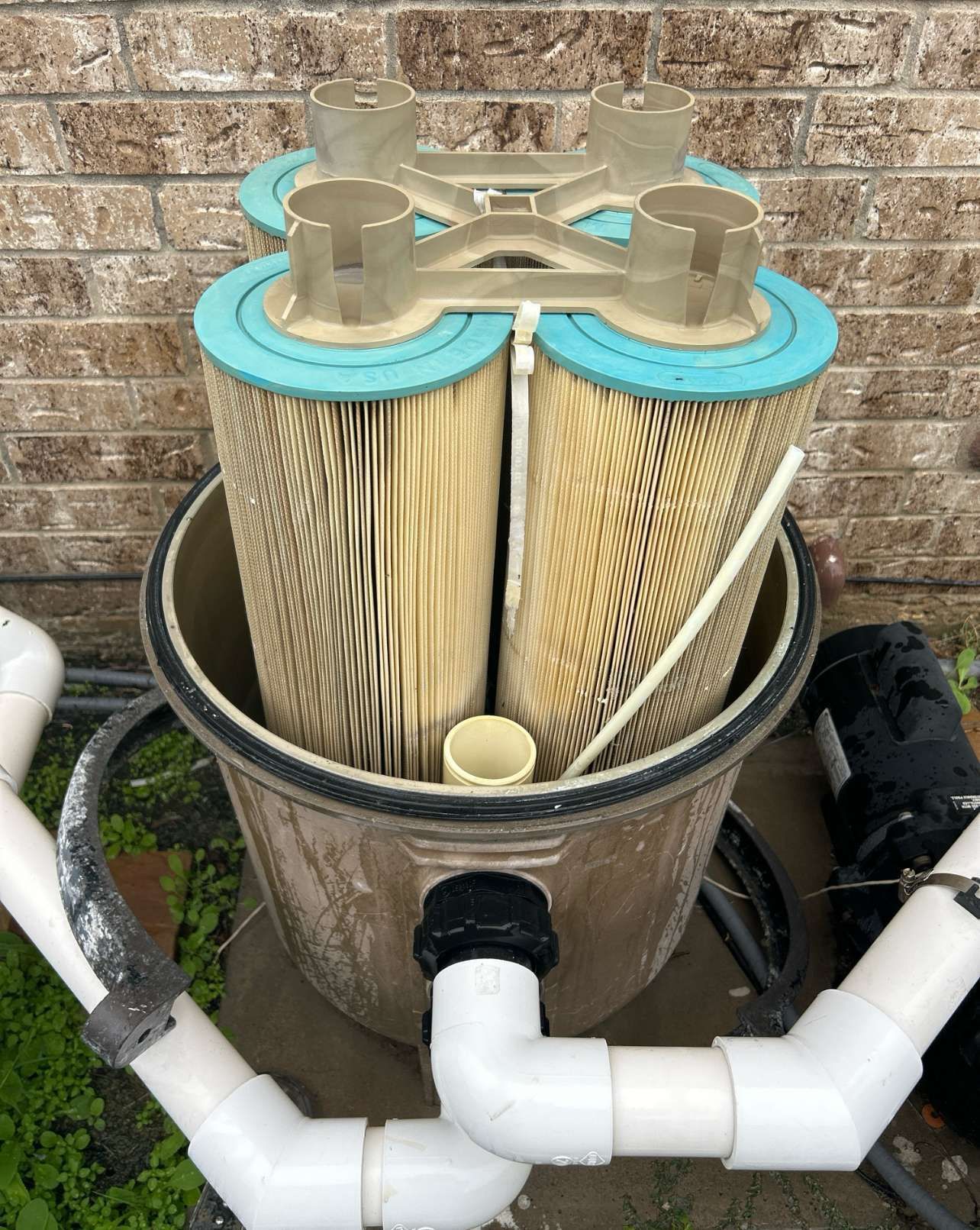 Pool filter with two tall cartridge filters inside a cylindrical housing, plumbing attached.