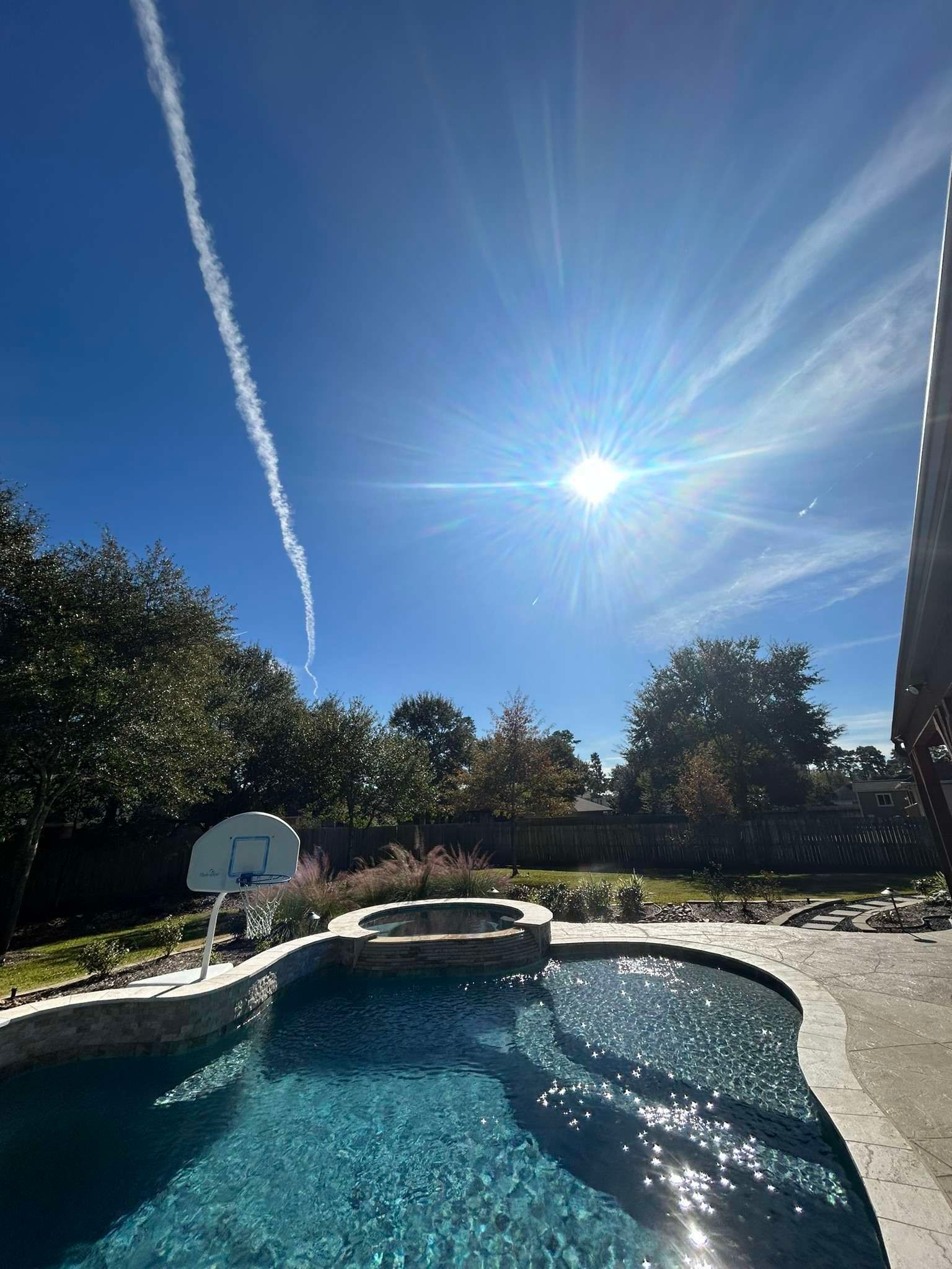 Pool area with a bright sun, blue sky, and a contrail.