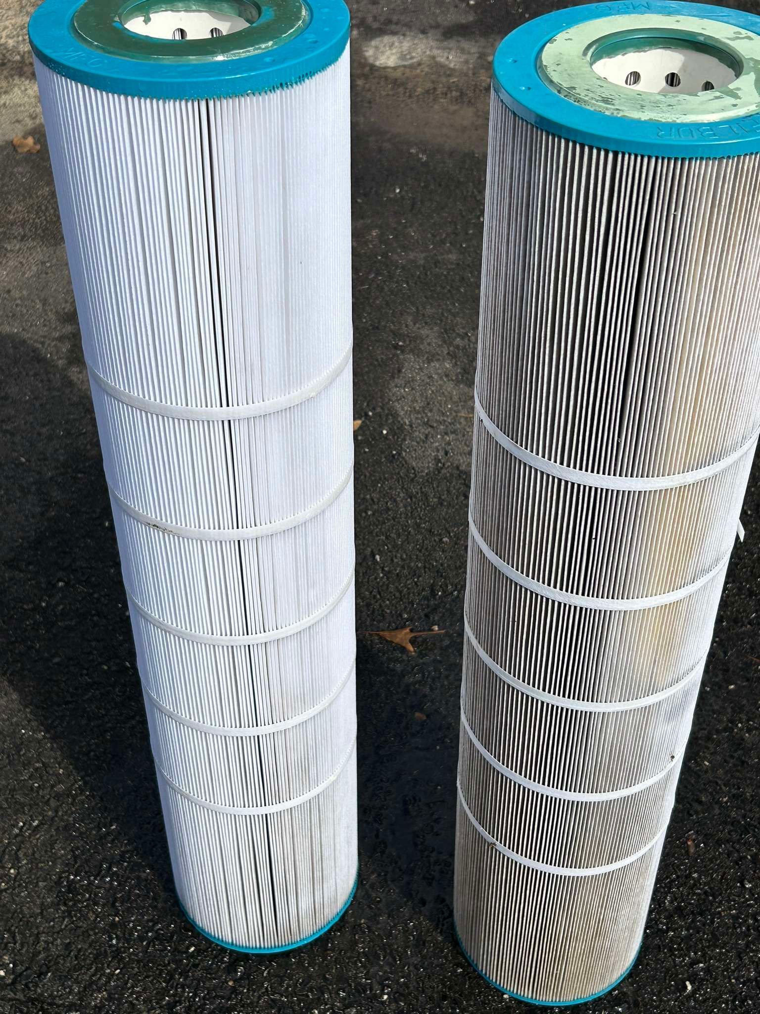Two cylindrical pool filters, one clean and one dirty, side-by-side on asphalt.